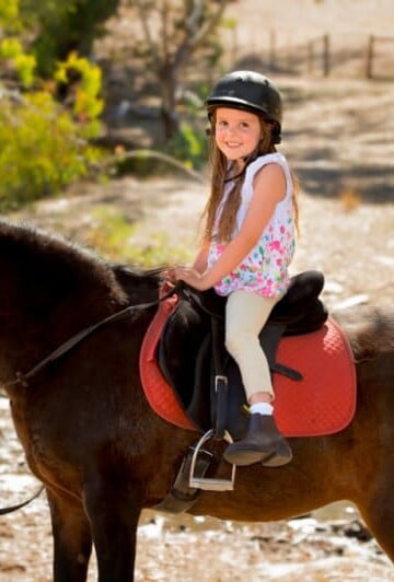Little girl wearing a helmet riding a horse