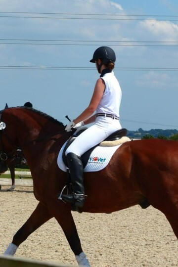 Woman in white riding pants and black boots riding a brown horse