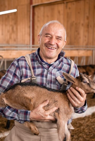Man holding a baby goat inside a barn
