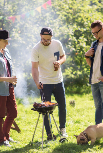 Three men with their dog grilling on a small grill