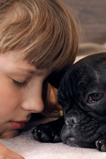 Little girl with eyes closed laying beside a sad black dog