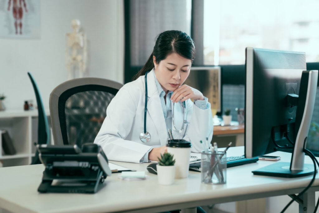 Doctor sitting at her desk writing on a pad in front of a monitor