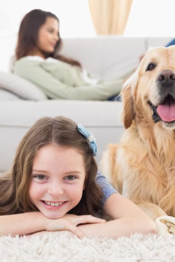 Small girl and dog laying on the floor in front of woman stretched out on a couch